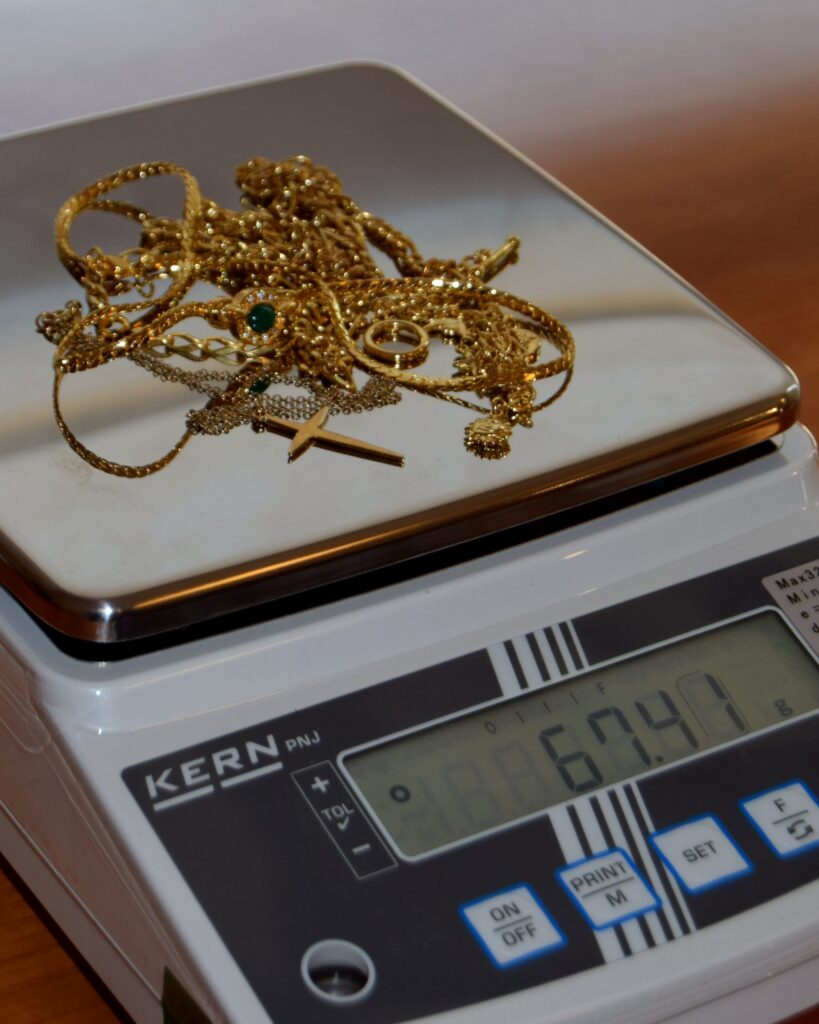 Gouden kettingen, een ring en een kruisje liggen op een digitale weegschaal