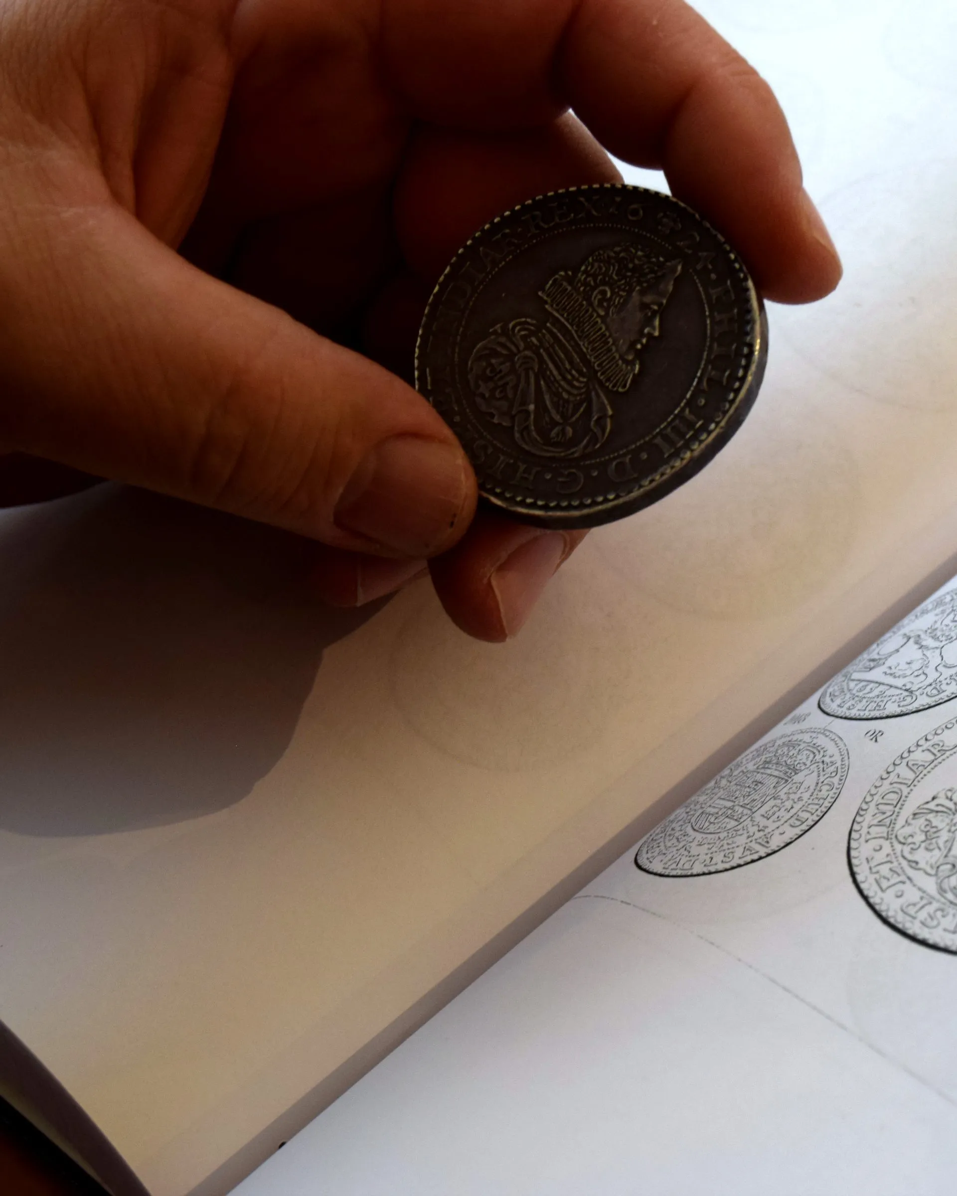 Een zilveren munt wordt naast de afbeeldingen in een muntcatalogus gehouden om jaartal en muntslag te vergelijken