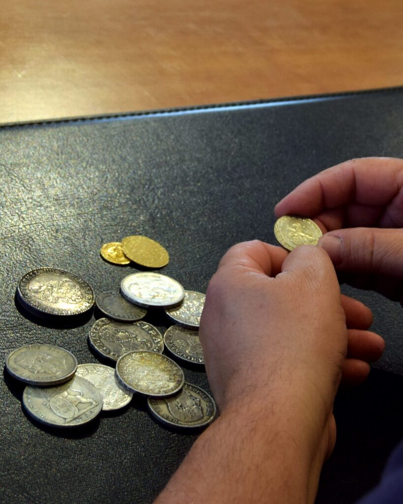 Een hand houdt een gouden munt vast boven zilveren en gouden munten op een zwarte onderlegger