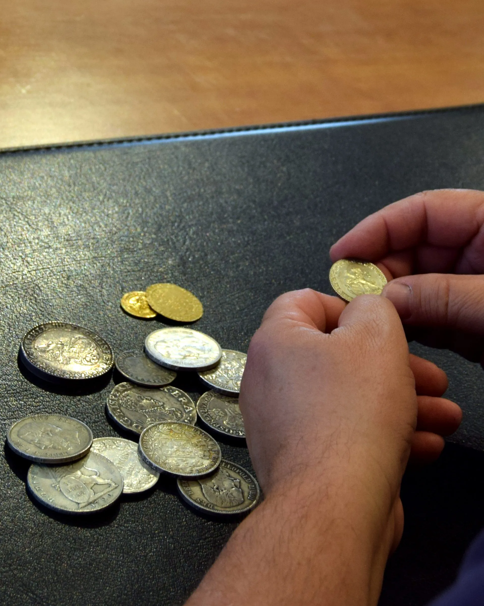 Een hand houdt een gouden munt vast boven zilveren en gouden munten op een zwarte onderlegger