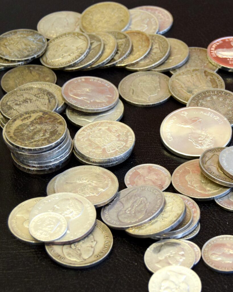 Stapels zilveren munten en enkele gekleurde herdenkingsmunten op een donkere tafel