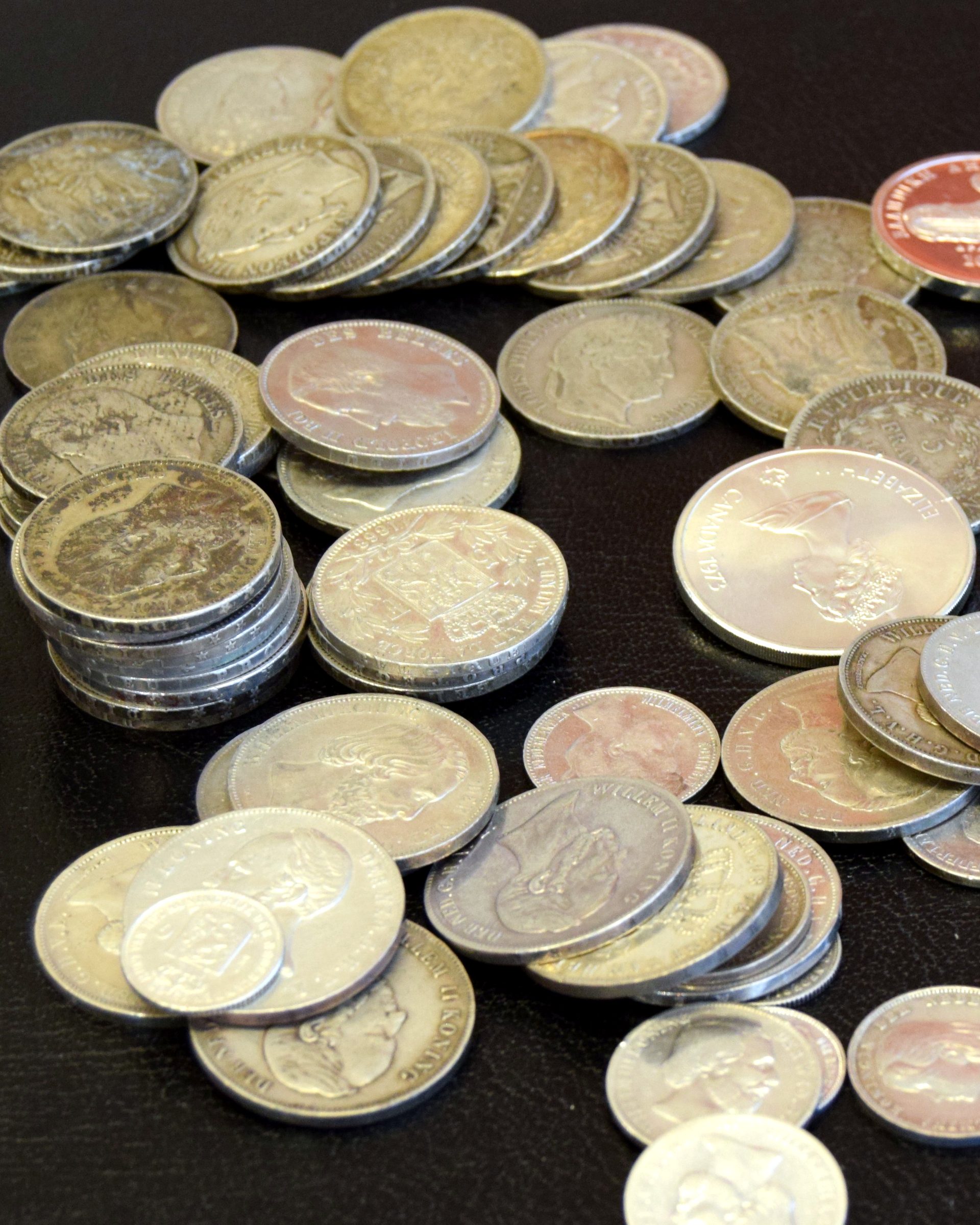 Stapels zilveren munten en enkele gekleurde herdenkingsmunten op een donkere tafel
